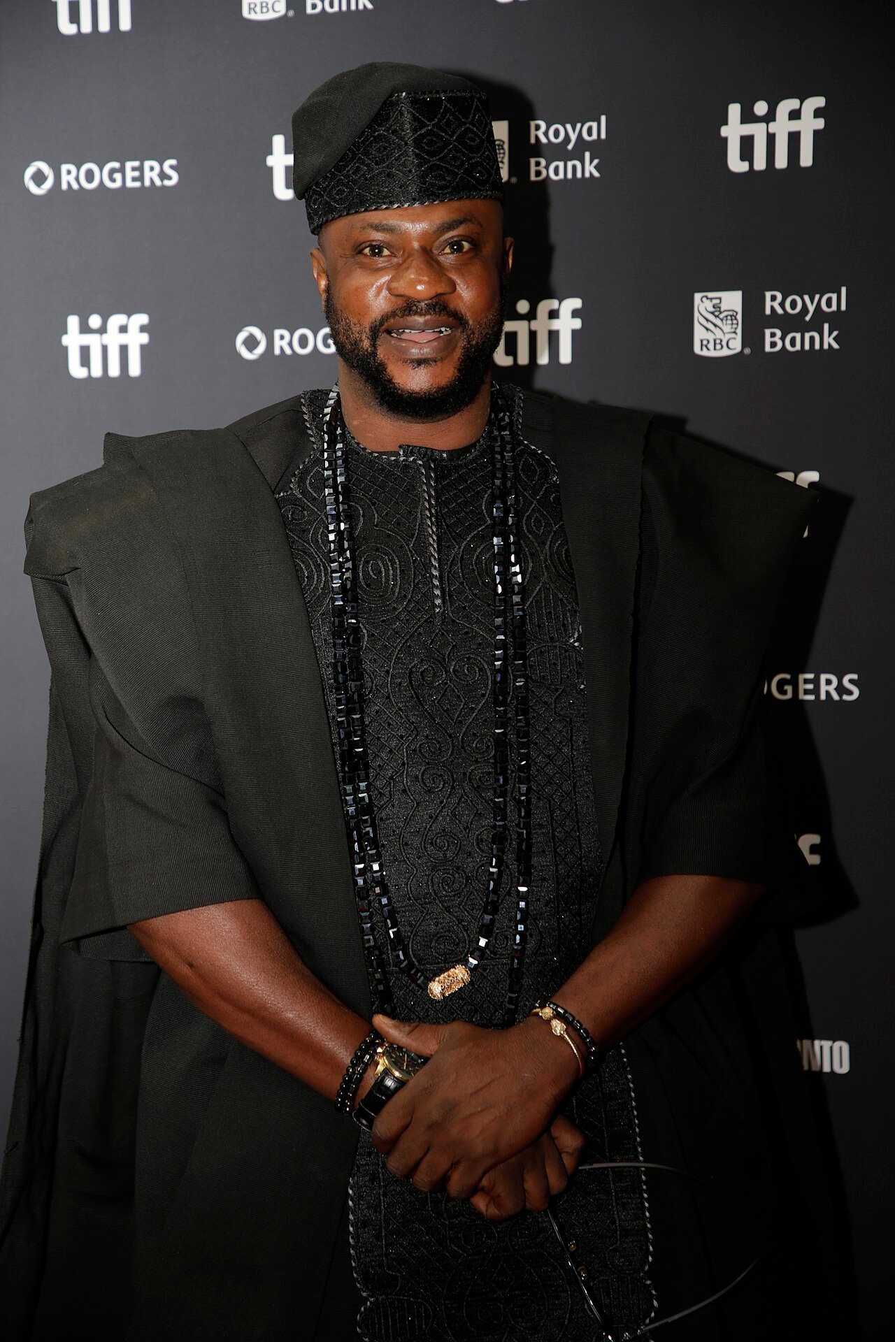 Odunlade Adekola in a black agbada, embroidered fila, and long beads, at the Toronto International Film Festival.
