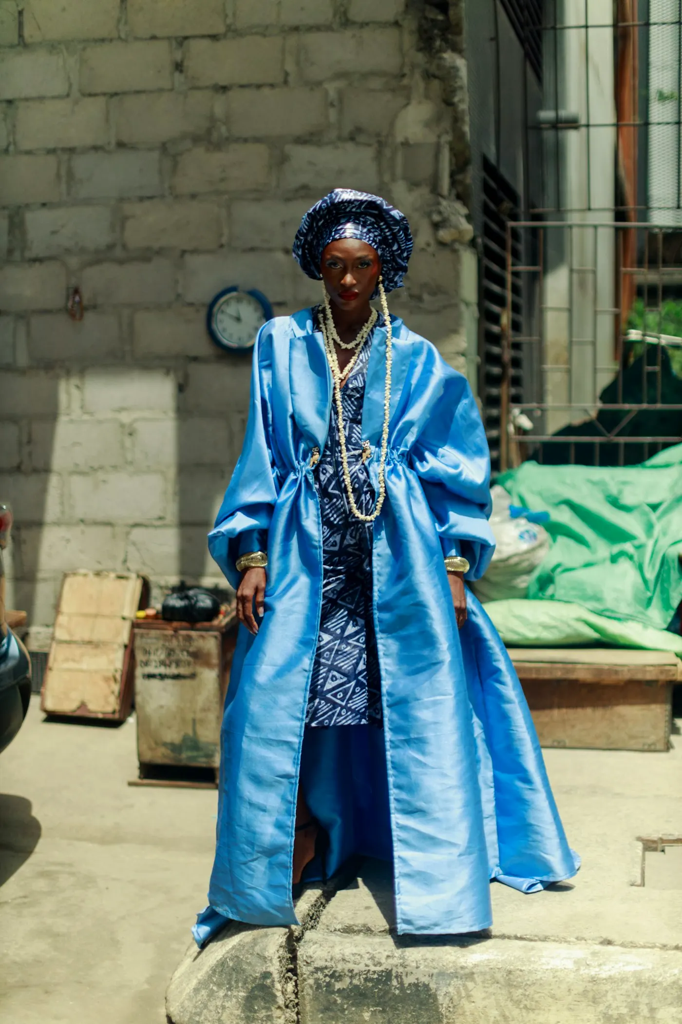 Fashion portrait of a woman in a blue satin coat and patterned headwrap.