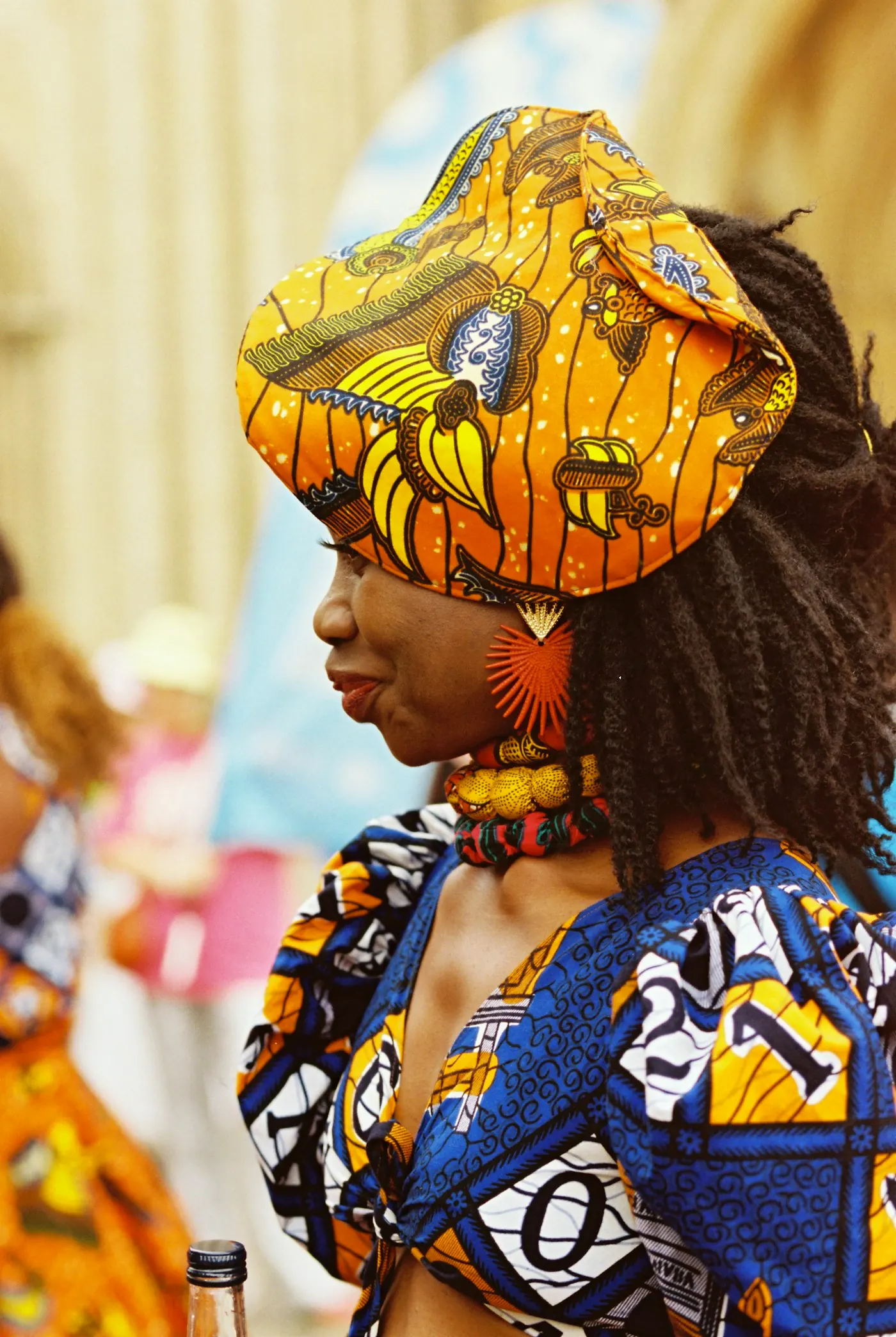 Woman in profile wearing a vivid wax-print headwrap and matching cloth.