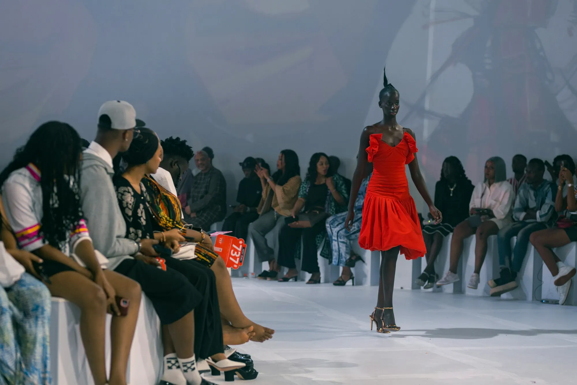A model in red crossing a runway while an audience watches.
